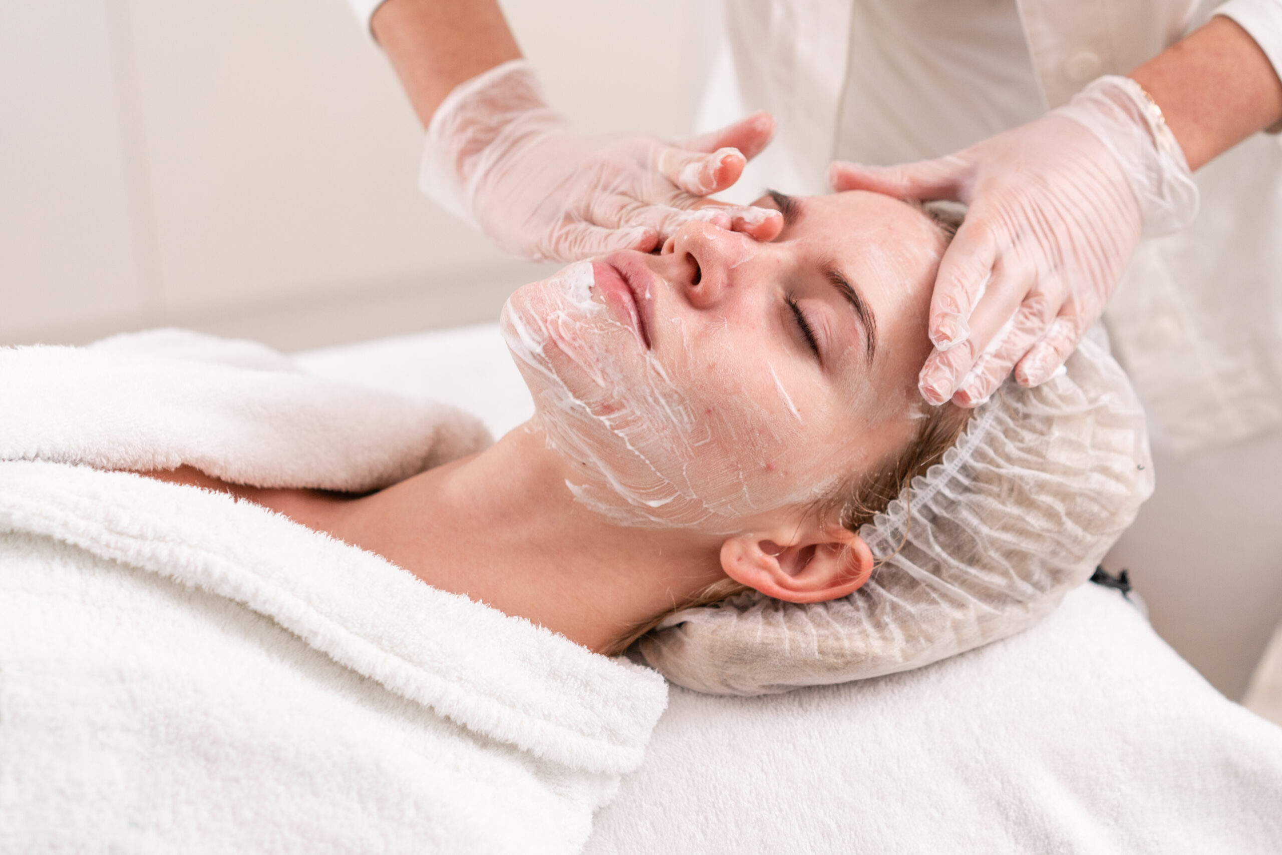 The Doctor Removes The Gel From The Patients Face And Apply A Therapeutic Cream. Anti Acne Phototherapy. Beautiful Woman During Photo Rejuvenation Procedure. Face Skin Treatment At Cosmetic Clinic.